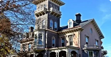 Victorian mansion with tower, ornate stone facade, and arched windows under blue sky.