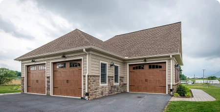 Custom detached garage with stone veneer, carriage-style wood doors, and brown shingle roof.