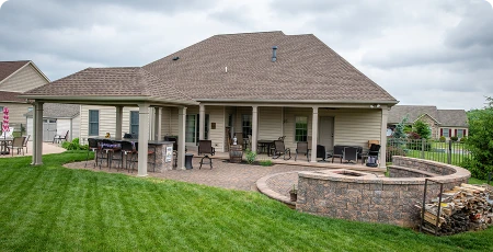 Suburban backyard patio with covered seating, dining table, and stone fire pit.